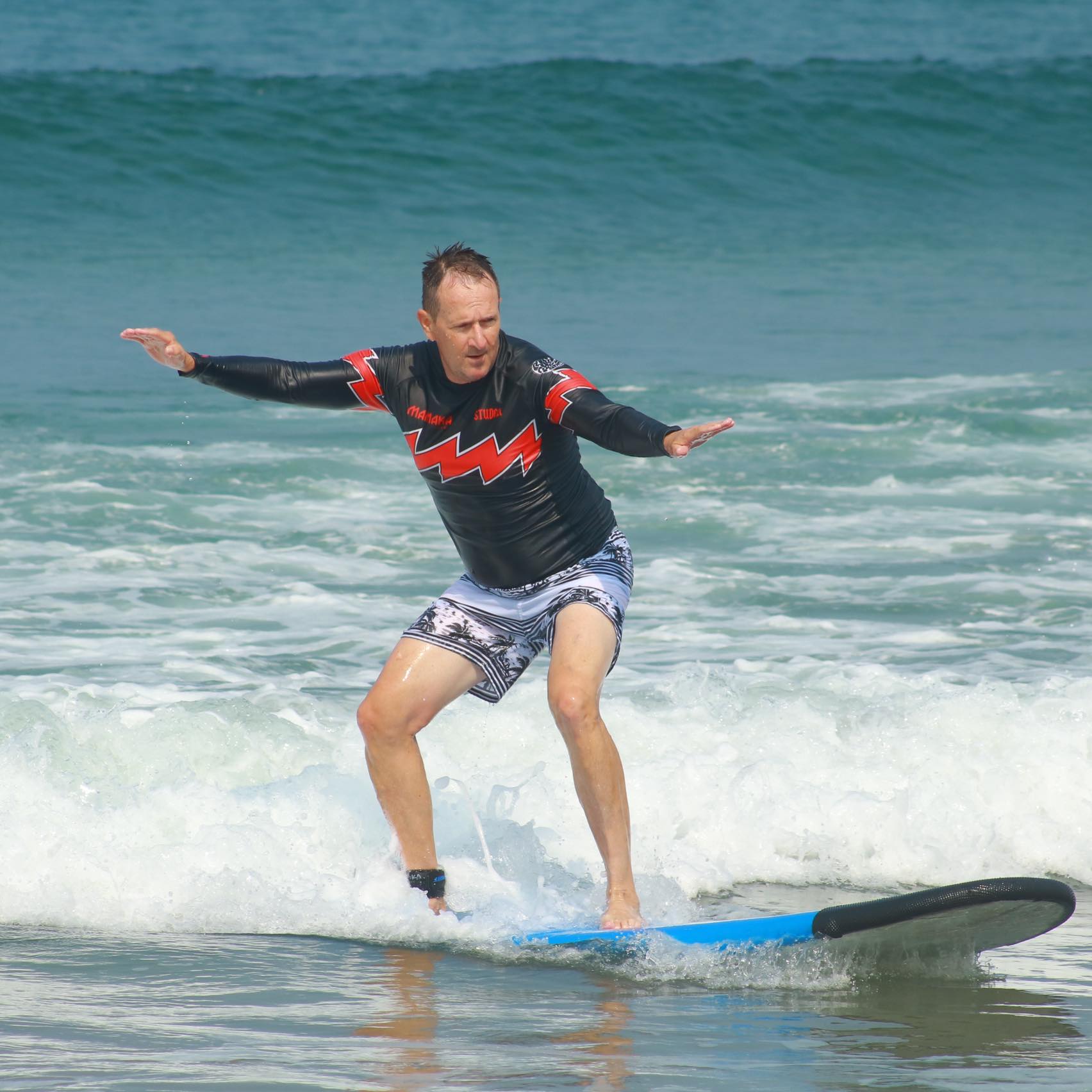 A man skillfully rides a surfboard on the waves of the ocean, showcasing his surfing prowess against a blue backdrop.