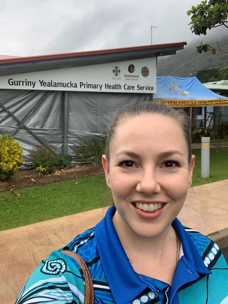 A woman wearing a blue shirt and blue shorts stands in front of a building, smiling confidently.