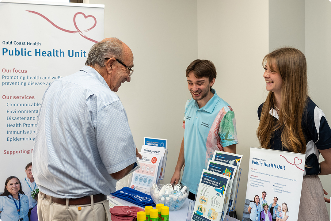 Two young people at a Public Health event talk to an older man with glasses. 