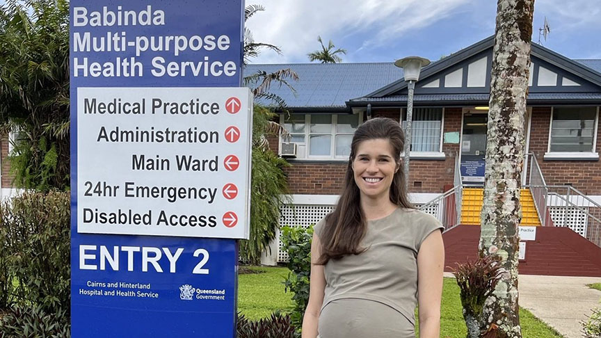 A pregnant woman stands before a Babinda Multipurpose Health Service sign, highlighting maternal health support in the community.