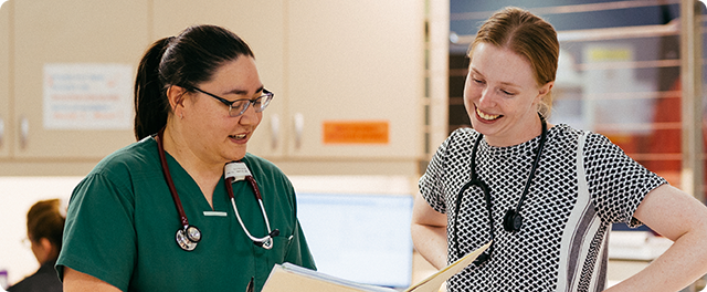 Two female doctors engaged in conversation at a desk, sharing insights in a professional healthcare setting.