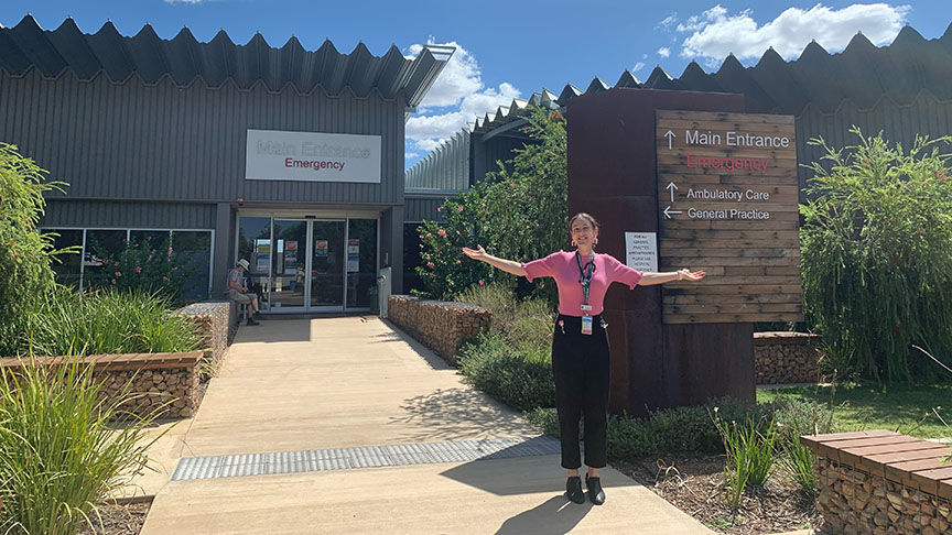 A woman stands with arms outstretched in front of a building, expressing joy and openness to her surroundings.