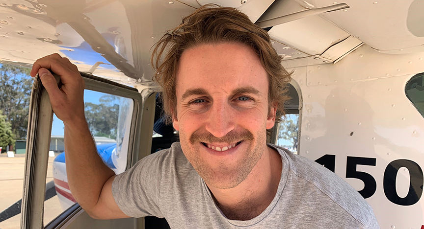 Tom Currie holding a small plane door and smiling to the camera.